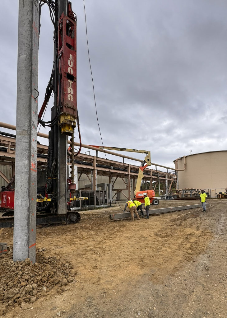 Workers and pile driving machine on construction site