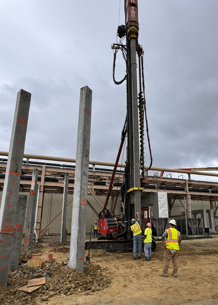 Workers and pile driving machine on construction site