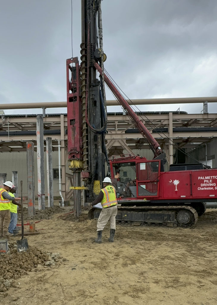 Workers and pile driving machine on construction site